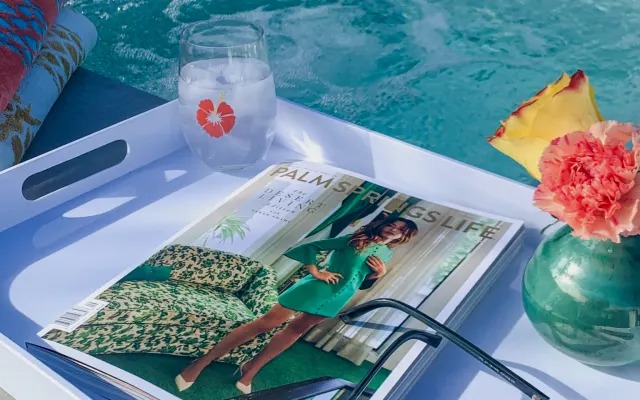 A cold drink and a Palm Springs Life magazine on a tray by the pool
